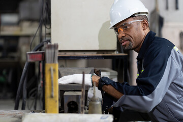 African American male engineer worker maintenance machine in the factory. Black male worker working with machine with safety uniform, goggles and helmet