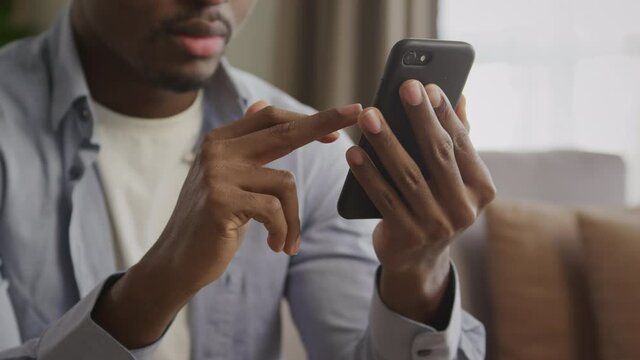 Close up of an unrecognisable african american young adult man swiping on a black smart phone