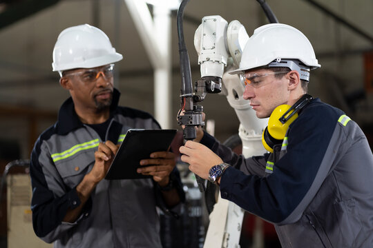 Group of male engineer worker maintenance automatic robotic arm machine in factory. Male technician worker checking, repair automatic robot hand machine with screwdriver in smart factory