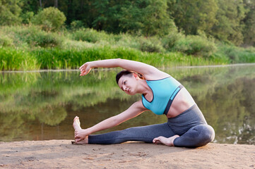 A young girl practices yoga on the lake in the park. Close up.