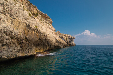 Fototapeta premium Sea side view of Siracusa coast cliffs, sandstone rocks and caves in sunny summer day. A bright colorful photo good for touristic booklet or book, boat trip ads, posters etc.