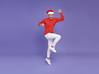 Fototapeta na wymiar Young asian man in red casual attire wearing Santa hat jumping with pointing finger aside front a copy space and smile face on purple background.Happy new year concept.