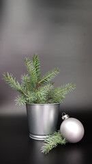 Christmas tree ball of silver color .next to it is a metal vase with fir twigs on a dark
