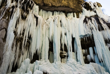 Fototapeta na wymiar Frozen waterfall with huge beautiful icicles hanging from the rocks. Chegem waterfalls - majestic spectacle of extraordinary beauty in Kabardino-Balkaria, Russia