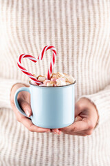 Girl in knitted wool sweater is holding a mug with hot chocolate with marshmallow.