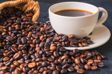 A cup of coffee and roasted coffee beans in a brown sack bag.