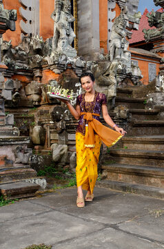 Portrait of beautiful Balinese girl inside old temple in Bali, with a traditional clothing and carrying offerings.