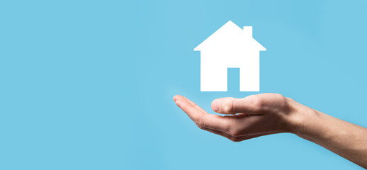 Male hand holding house icon on blue background. Property insurance and security concept.Real estate concept.Banner with copy space.