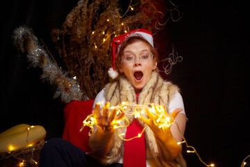 A cheerful dwarf with garlands in his home. Assistant of Santa Claus in a red hat and with glowing garlands. A middle-aged or elderly woman poses in the studio like a fairy-tale character