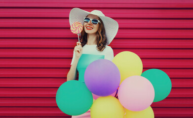 Portrait of beautiful happy smiling young woman with bunch of balloons wearing a colorful dress on pink background