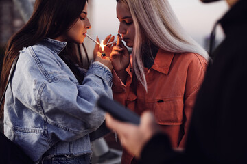 Two rebellious teenage girls are standing outdoors and lighting cigarettes. Teenagers smoking.