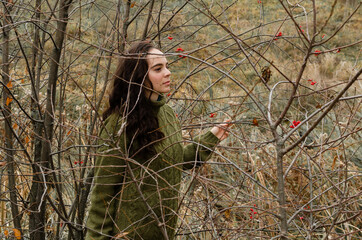 Dreamy brunette young woman stands in the forest surrounded by tree brunches. One with nature concept.