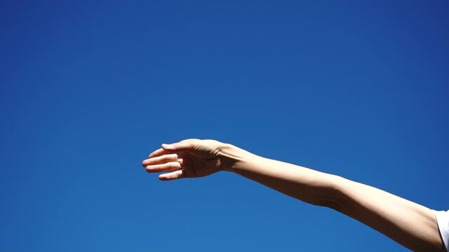 白い紙ひこうきを飛ばす女性の手元 青空背景