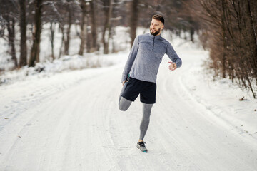 Sportsman doing stretching exercises and preparing to run in nature at snowy winter day. Winter...