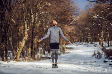 Fototapeta na wymiar Fit sportsman jumping the rope in woods at snowy sunny winter day. Winter fitness, cardio exercises