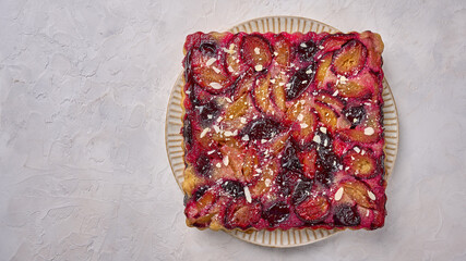 Traditional pie with plums on plate on light wooden background. Top view. Copy space