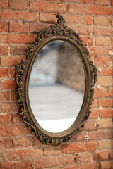 A mirror in a vintage openwork frame hangs on an old brick wall