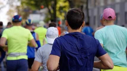 Crowd of people running marathon, focus on man with earphones. Contestants of sports competition. Concept of healthy lifestyle