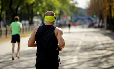Muscular man wearing black sportswear and yellow headband approaching finish line at city marathon,...