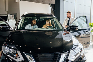 Multi ethnic couple choosing new car at modern showroom