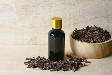 Essential oil of cloves in bottle and dry cloves on wooden bowl on rustic wooden background.