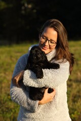 Small and cute black Cocker Spaniel puppy in the human hug, morning sun.