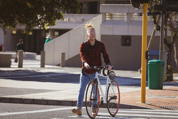 Thoughtful albino african american man with dreadlocks crossing street with bike