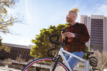 Happy albino african american man with dreadlocks on bike using smartphone