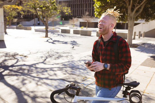 Happy albino african american man with dreadlocks on bike using smartphone