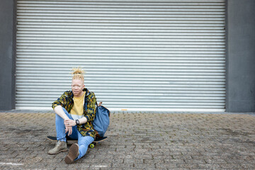 Portrait of thoughtful albino african american man with dreadlocks sitting skateboard