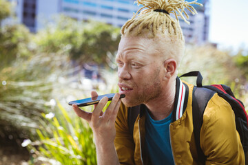 Happy albino african american man with dreadlocks in park talking on smartphone