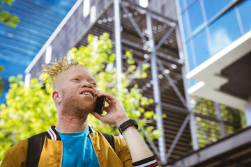 Happy albino african american man with dreadlocks in park talking on smartphone