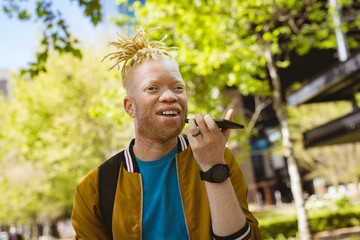 Happy albino african american man with dreadlocks in park talking on smartphone