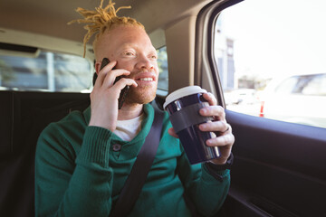 Happy albino african american man with dreadlocks sitting in car talking on smartphone