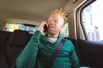 Happy albino african american man with dreadlocks sitting in car talking on smartphone