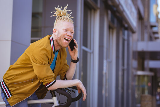 Happy albino african american man with dreadlocks talking on smartphone