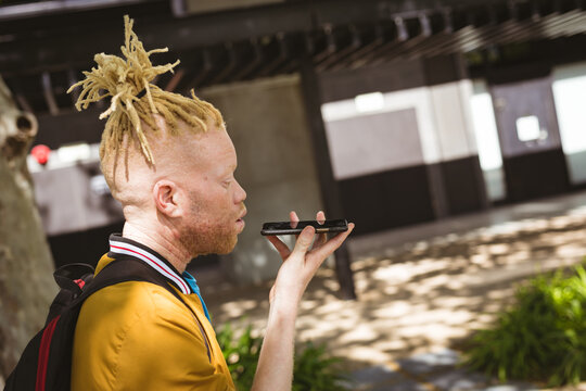 Happy albino african american man with dreadlocks on street talking on smartphone