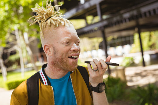 Happy albino african american man with dreadlocks in park talking on smartphone