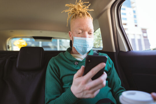 Albino african american man wearing face mask sitting in car using smartphone - Powered by Adobe