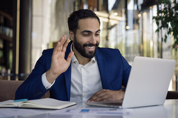 Handsome smiling arabic businessman using laptop computer having video call working in modern office. Happy middle eastern student studying distance learning. Online lesson concept 