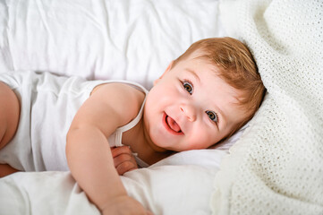 Obraz premium A smiling baby lying on a white blanket.