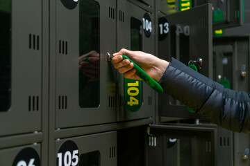 Close-up of a woman's hand opens or closes a numbered storage box in a public place. Cells are dark in color with metal locks and green-yellow keys with numbers. Temporary storage of things