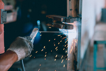 A steelworker is welding a structure in a factory with safety equipment. The concept of maintenance of construction with skilled labor.
