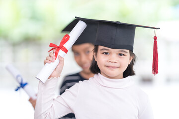 Happy Asian female school kid graduates with a graduation cap hold a rolled certificate celebrate...