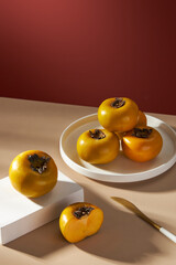 Front view of white circle , square podium with dish of persimmon in red background for food advertising 