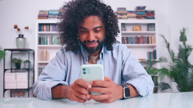 Happy smiling bearded Middle Eastern millennial male hold smart phone use business entertainment application engaged in online chat. Modern day young man addicted to gadget. Surfing virtual world.