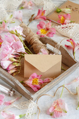 Blank envelope on a wooden tray between pink flowers