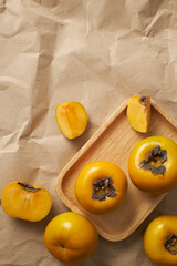 Top view of wooden tray of persimmon in brown draft paper background for food advertising 