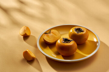 Front view of a yellow dish with persimmon in almond background for food advertising 