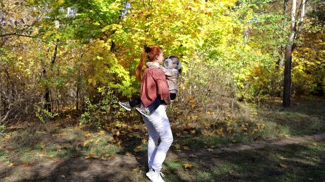 a red-haired happy woman with a little daughter in her arms in an autumn sunny park